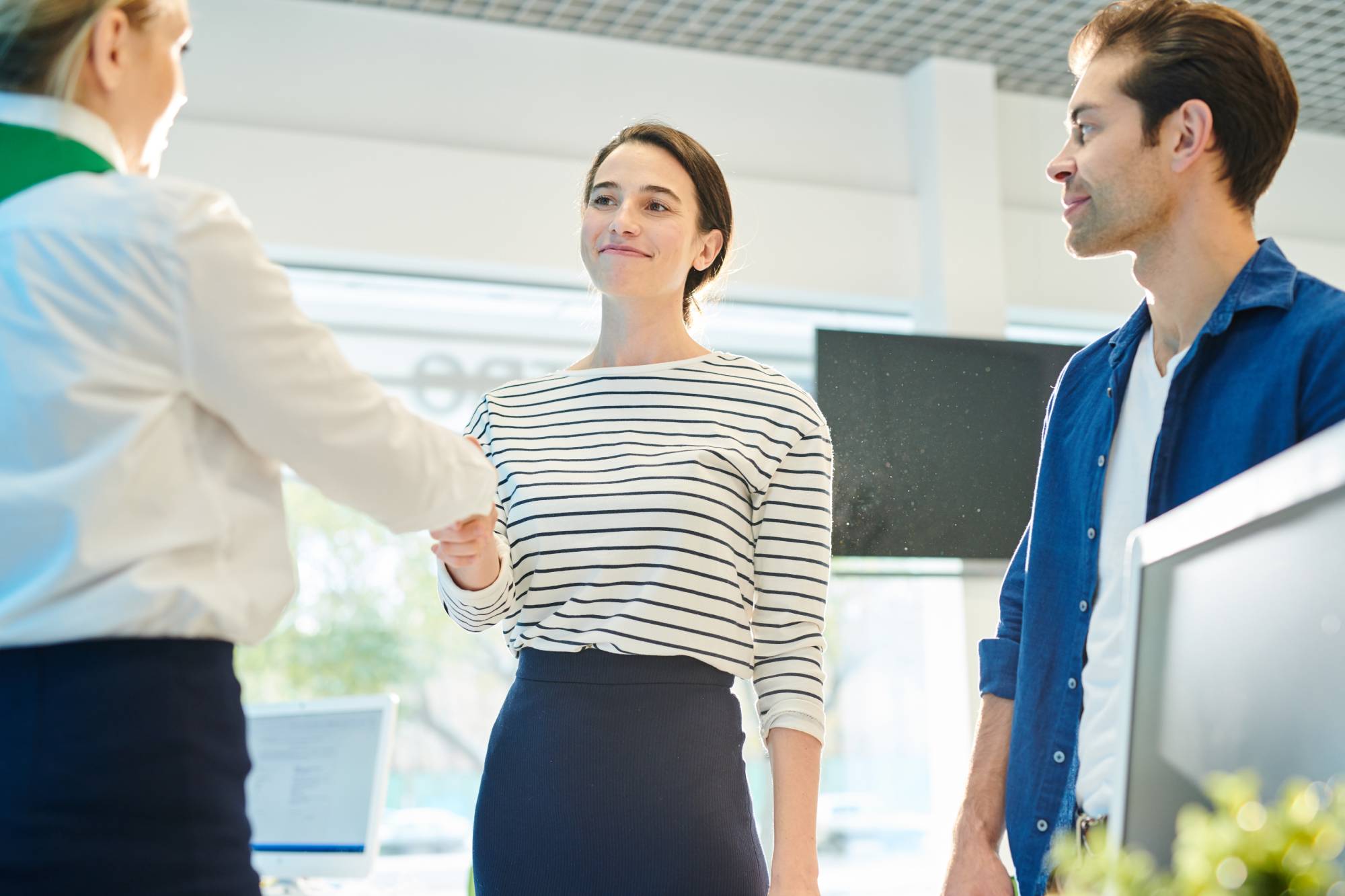 Zufriedene, selbstbewusste, attraktive junge Dame im ausgezogenen Pullover, die die Hand des persönlichen Managers schüttelt, während sie sich mit ihr im Büro trifft, junges Paar, das einen Deal mit einem Makler abschließt